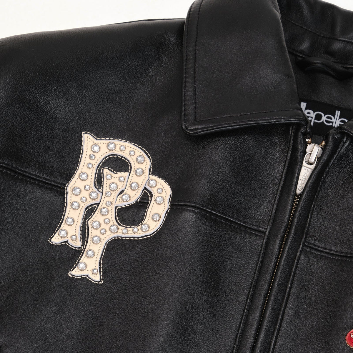 Women's black leather eagle patch bomber jacket, close-up of cream chest monogram, silver-tone embellishments and zip closure.