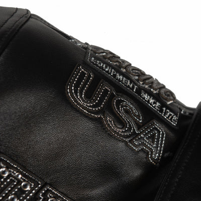 Close-up of black leather racing jacket shoulder showing USA lettering, layered applique and contrasting silver-tone stitched details.