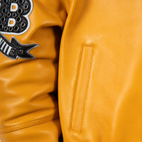 Lower front pocket detail of yellow leather jacket showing angled welt opening, neat stitching and part of the embellished sleeve patch.