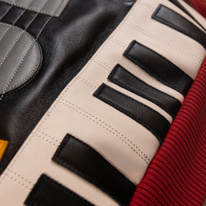 Lower back detail of leather music jacket showing stitched ivory and black piano-key applique above a deep red ribbed waistband.