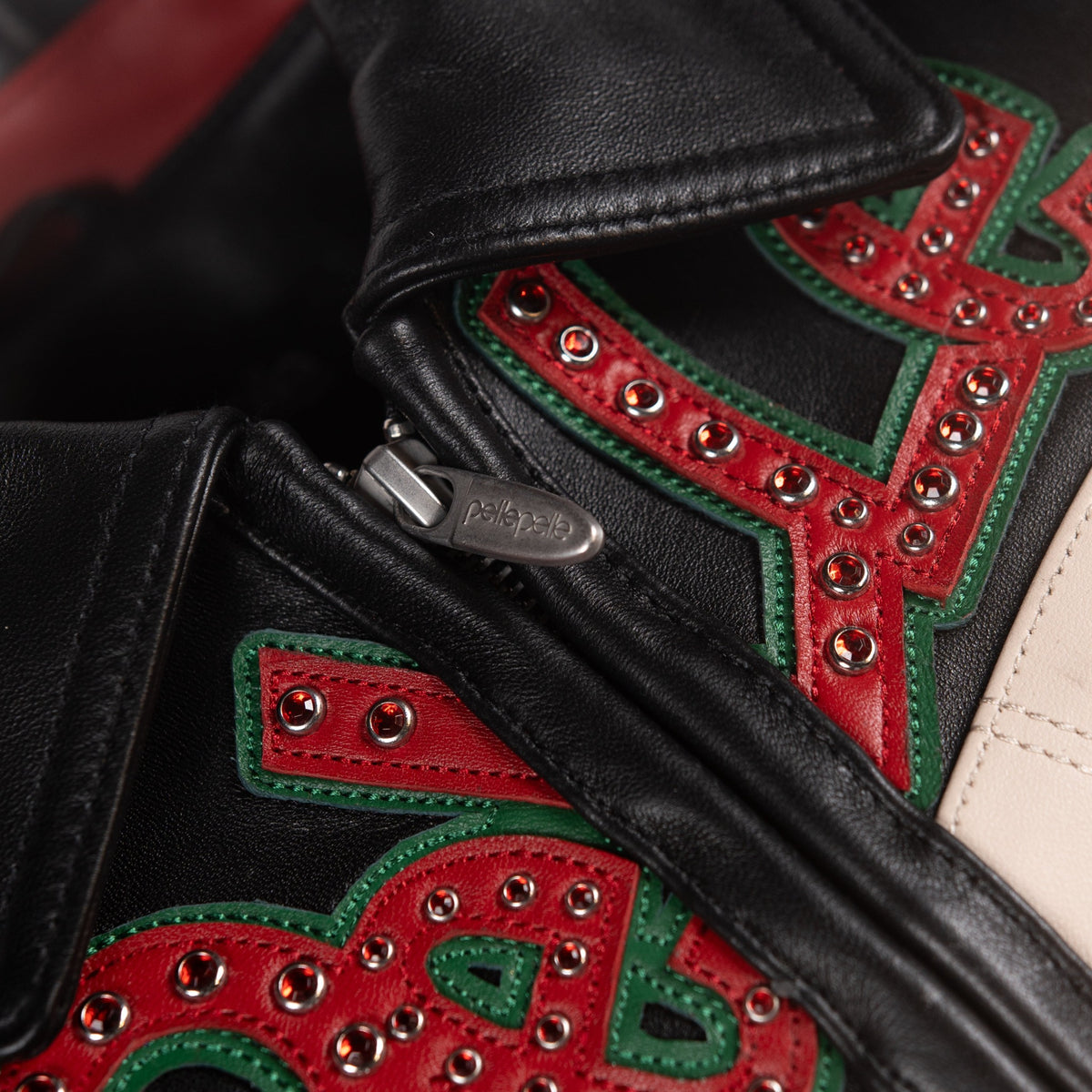 Close-up of black leather jacket collar and zipper with layered red and green lettering and rows of red decorative embellishments.