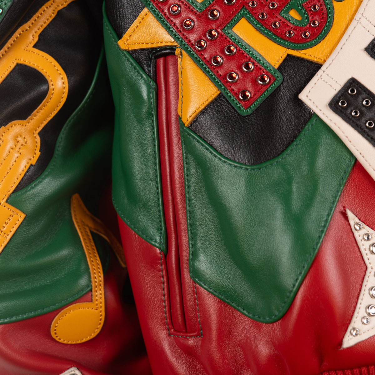 Detail of red welt pocket on multicolor leather music jacket, framed by green panels, yellow applique and jeweled lettering details.