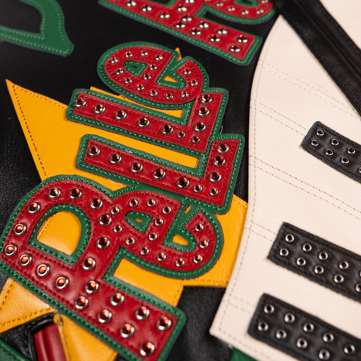 Close-up of layered red and green lettering on black leather music jacket beside ivory piano keys and silver-tone eyelet accents.