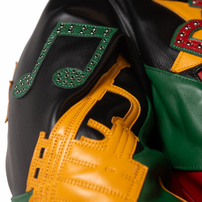 Sleeve detail of multicolor leather jacket showing a green musical note with decorative stones and a yellow trumpet-shaped applique.