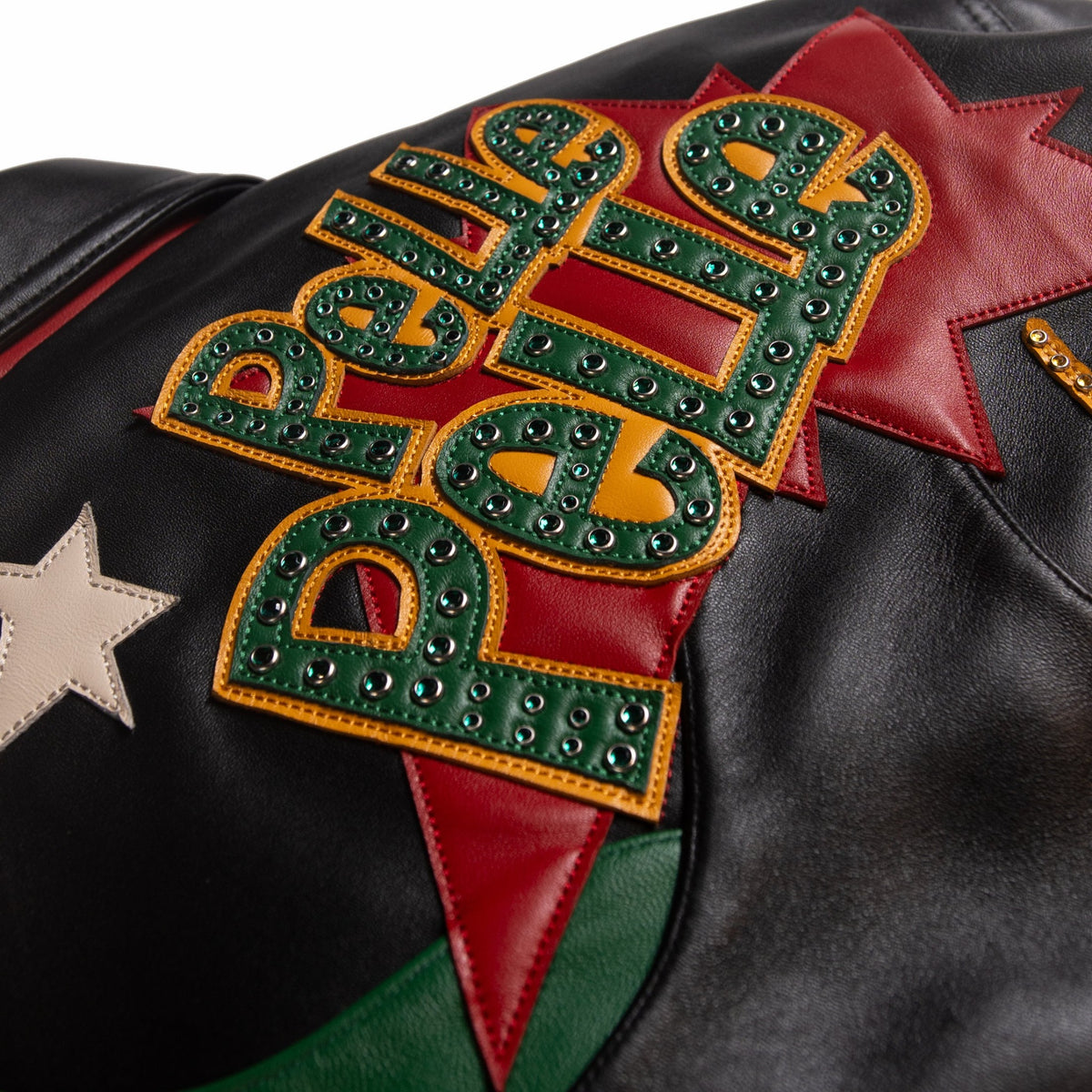 Back applique detail of multicolor leather music jacket with green jeweled lettering, yellow edging and a red starburst background.