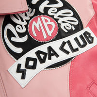 Chest patch detail of pink leather jacket with black circular applique, white script, pink monogram center and white lettering banner.