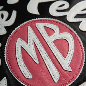 Close-up of pink monogram circle on black leather jacket applique with layered white initials and stitched edges in contrasting thread.